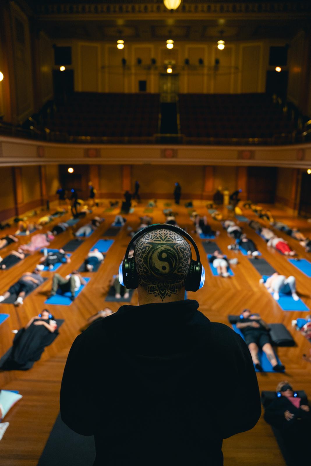 A real 9D breathwork session at a Hope Cartel event — a facilitator with headphones overlooking a hall of attendees lying on mats