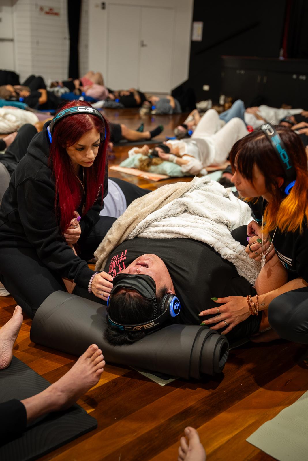 A facilitator tending to a participant lying down with an eye mask and headphones during a Hope Cartel session