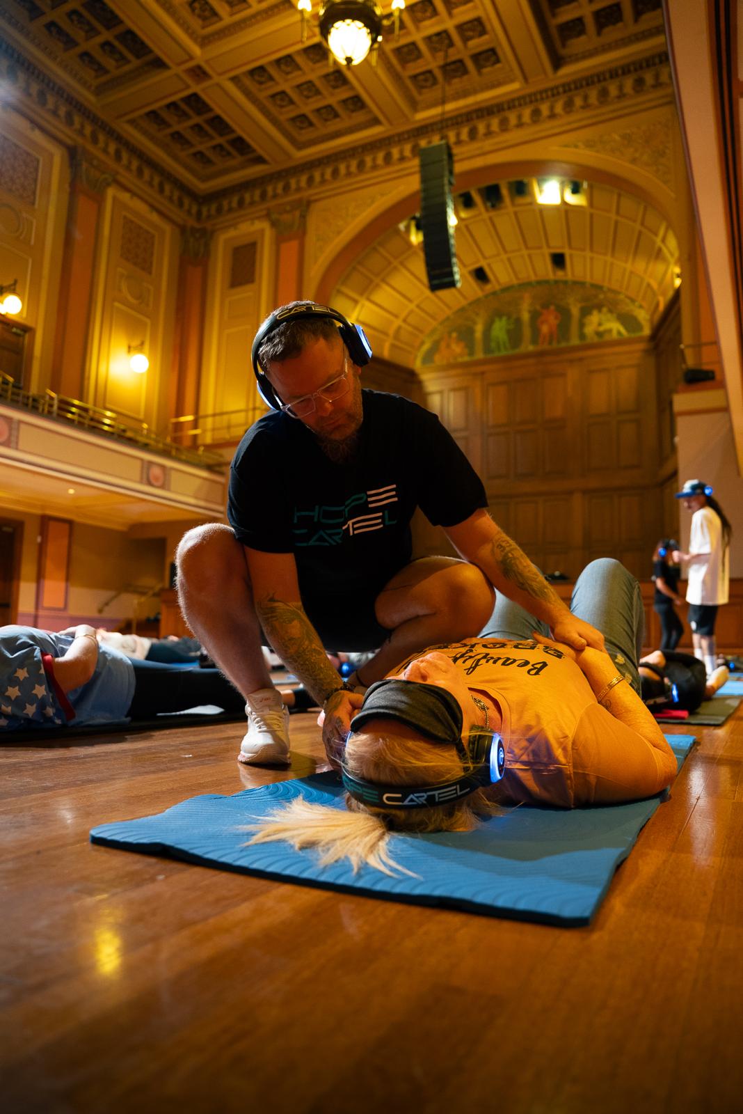 Facilitator supporting a participant lying on a mat in an ornate hall during a 9D breathwork session