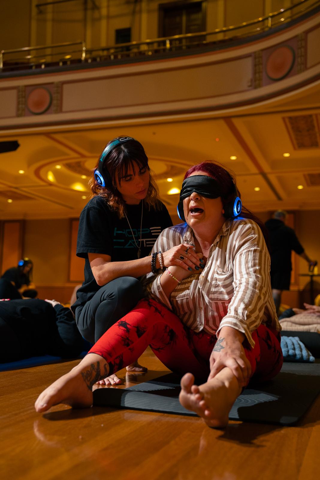 Facilitator comforting a blindfolded participant mid-session in a grand hall