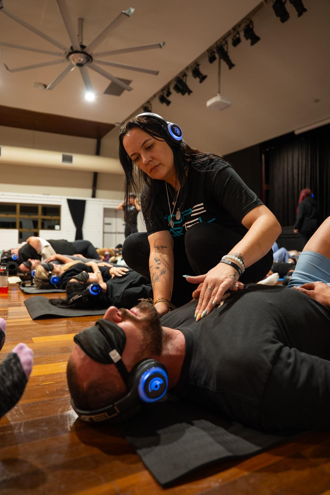 Facilitator placing hands on a participant lying down with headphones during a session